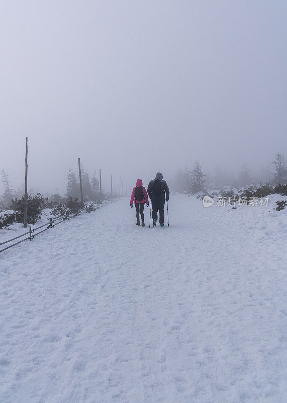 一个男人和一个女人走过一片雪景。由于大雾和大雪，能见度很低。冬季从斯涅兹卡(Snezka)山看，巨型山脉。Karkonosze (Krkonose)
